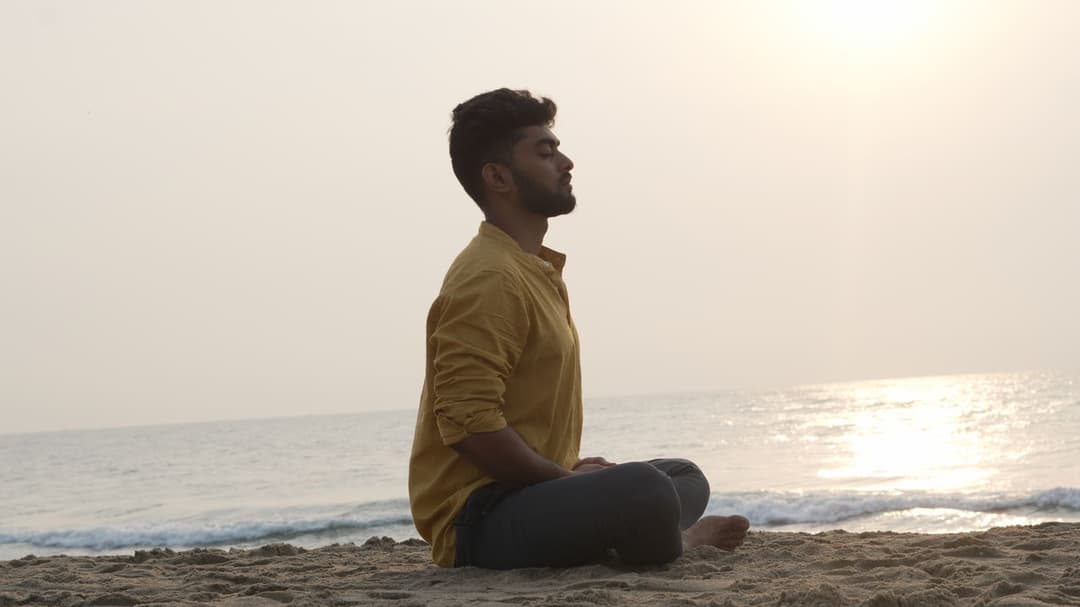 A man meditating on the beach at sunrise