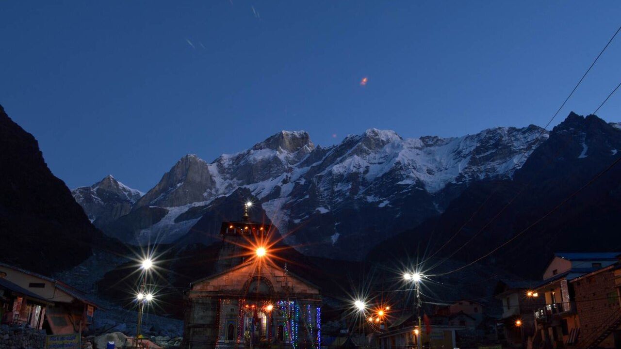 Kedarnath temple lit up at dawn below snow covered Himalayan peaks