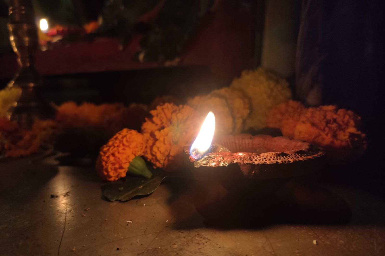 A lit clay oil lamp with marigold flowers at a home altar before dawn