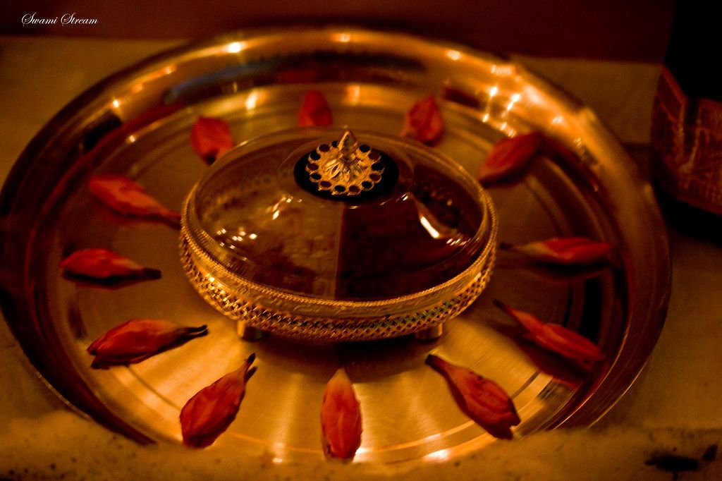 A brass pooja thali with flower petals arranged around a small lamp
